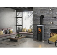 Moderner Kaminofen in einem hellen Wohnzimmer im Industrial-Stil mit Sichtbetonwänden und großem Fenster.