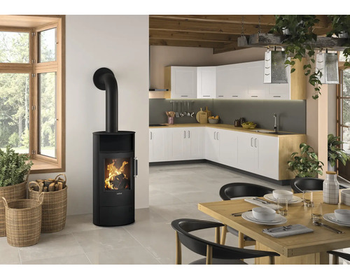 Moderner schwarzer Kaminofen mit sichtbarem Feuer in einer hellen Küche mit Essbereich, weißen Schränken und Holzoberflächen.