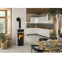 Moderner Kaminofen mit weißer Verkleidung und brennendem Feuer in einer hellen, offenen Küche mit Essbereich und Holzbalkendecke.