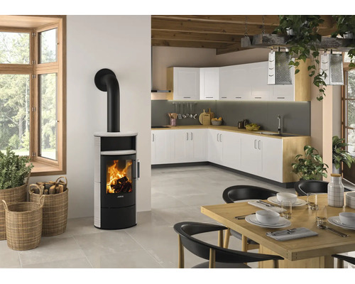 Moderner Kaminofen mit weißer Verkleidung und brennendem Feuer in einer hellen, offenen Küche mit Essbereich und Holzbalkendecke.