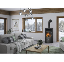 Modern eingerichtetes Wohnzimmer mit schwarzem Kaminofen Justus, grauem Sofa, Holztisch und großen Fenstern mit Blick auf eine verschneite Winterlandschaft.