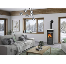 Moderner Wohnraum mit freistehendem Kaminofen aus schwarzem Stahl mit weißer Verkleidung, grauem Sofa, Holztisch und großen Fenstern.