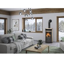 Moderner Kaminofen aus schwarzem Metall und Holz in einem hellen Wohnzimmer mit grauem Sofa und großen Fenstern mit Bergblick.