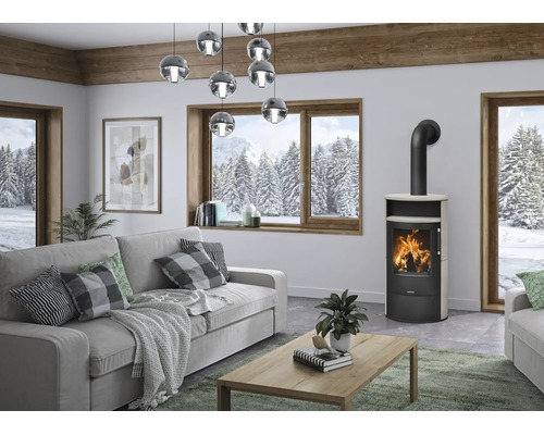 Moderner Kaminofen in einem hellen Wohnzimmer mit grauem Sofa, Holztisch und Blick auf eine verschneite Waldlandschaft.