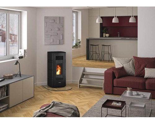Moderner heller Wohnbereich mit schwarzem Pelletofen, brennendem Feuer, Fischgrät-Parkett, rotem Sofa und erhöhtem Küchenbereich im Hintergrund.