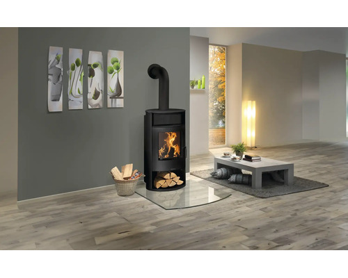 Moderner schwarzer Kaminofen in einem hellen Wohnzimmer mit Holzboden, Glasbodenplatte und Korb mit Brennholz.