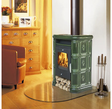 Kaminofen mit Kachelverkleidung und loderndem Feuer in einem gemütlich eingerichteten Wohnzimmer mit Holzmöbeln und Kaminbesteck.