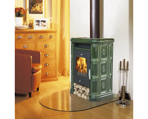 Kaminofen mit Kachelverkleidung und loderndem Feuer in einem gemütlich eingerichteten Wohnzimmer mit Holzmöbeln und Kaminbesteck.