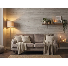 Wohnzimmer mit Wandpaneelen in Holzoptik, einem Sofa mit Kissen und Decken, einer Stehlampe und einem Wandregal.