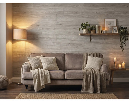 Wohnzimmer mit Wandpaneelen in Holzoptik, einem Sofa mit Kissen und Decken, einer Stehlampe und einem Wandregal.