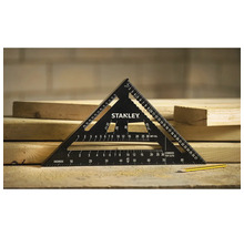 Schwarzer Stanley Sparrenwinkel aus Metall mit Messskalen auf hellen Holzbohlen liegend, daneben ein gelber Bleistift in einer hellen Werkstatt.