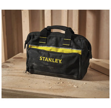 Stanley Werkzeugtasche aus schwarzem und gelbem Stoff mit Tragegriff auf einer hölzernen Werkbank mit Holzspänen in einer Werkstatt.