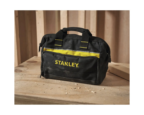 Stanley Werkzeugtasche aus schwarzem und gelbem Stoff mit Tragegriff auf einer hölzernen Werkbank mit Holzspänen in einer Werkstatt.