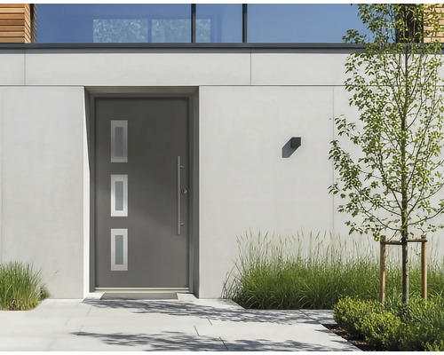 Moderne Hauseingangstür in Anthrazit mit drei Lichtausschnitten und langem Edelstahlgriff in einer hellen Fassade mit Bepflanzung.
