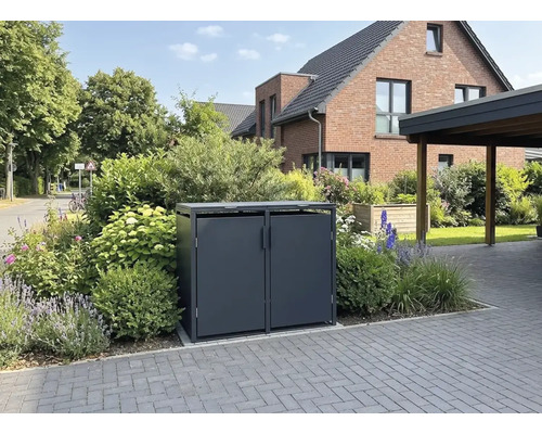 Dunkelgraue Metall-Mülltonnenbox für zwei Mülltonnen in einem bepflanzten Vorgarten an einer gepflasterten Einfahrt.