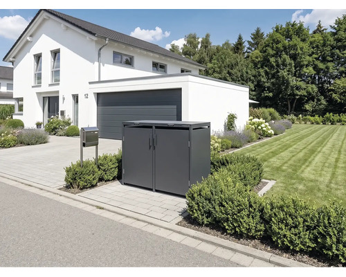 Moderne Mülltonnenbox aus Metall für zwei Tonnen in Anthrazit vor einem weißen Haus mit gepflasterter Einfahrt und Rasenfläche.