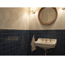 Klassisches Badezimmer mit dunkelblauen Wandfliesen, weißem Keramik-Waschbecken mit Messingarmaturen, rundem Spiegel und hellen Wänden.