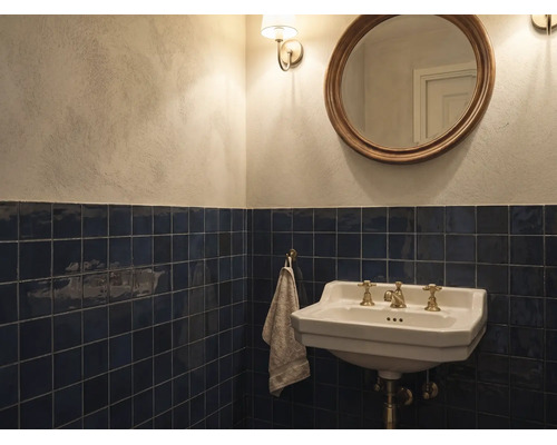 Klassisches Badezimmer mit dunkelblauen Wandfliesen, weißem Keramik-Waschbecken mit Messingarmaturen, rundem Spiegel und hellen Wänden.