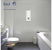 Moderner, heller Badezimmerraum mit wandmontiertem Durchlauferhitzer, Badewanne, Toilette und Waschbecken. Hergestellt in Deutschland.