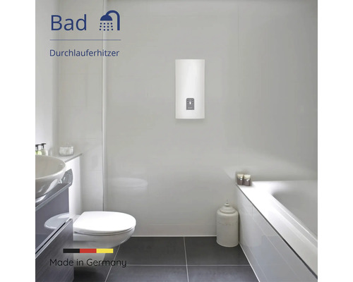 Moderner, heller Badezimmerraum mit wandmontiertem Durchlauferhitzer, Badewanne, Toilette und Waschbecken. Hergestellt in Deutschland.