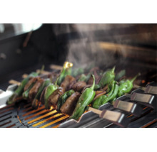 Fleisch und grüne Paprika auf Metallspießen über einem heißen Grillrost mit aufsteigendem Dampf.