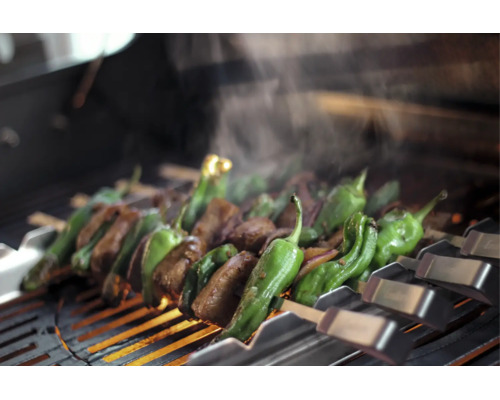 Fleisch und grüne Paprika auf Metallspießen über einem heißen Grillrost mit aufsteigendem Dampf.