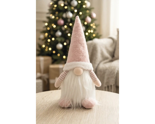 Stoffwichtel mit spitzer Mütze und Bart auf einem Holztisch in einem hellen, festlich dekorierten Raum mit geschmücktem Weihnachtsbaum.
