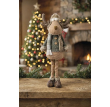Dekorative Rentier-Figur aus Stoff mit langen Beinen und Winterkleidung in einem festlich dekorierten Raum mit beleuchtetem Weihnachtsbaum und Kamin.