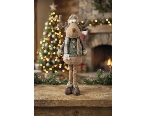 Dekorative Rentier-Figur aus Stoff mit langen Beinen und Winterkleidung in einem festlich dekorierten Raum mit beleuchtetem Weihnachtsbaum und Kamin.