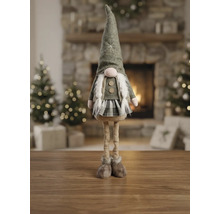 Dekorativer Weihnachtswichtel mit langen Beinen, Filzhut und kariertem Rock auf Holzoberfläche in hellem Wohnzimmer mit Kamin und Weihnachtsbäumen.