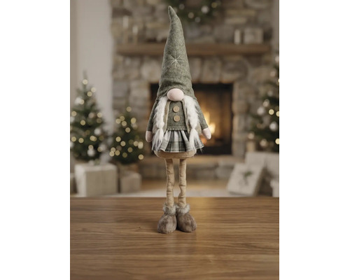 Dekorativer Weihnachtswichtel mit langen Beinen, Filzhut und kariertem Rock auf Holzoberfläche in hellem Wohnzimmer mit Kamin und Weihnachtsbäumen.