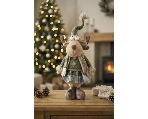 Weihnachtsfigur Rentier aus Textil mit grünem Pullover, kariertem Rock und spitzem Hut, stehend auf einem Tisch vor einem Weihnachtsbaum.