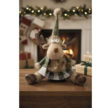 Plüsch-Rentier mit spitzem Hut, Schal und kariertem Rock als Weihnachtsdekoration auf einem Holztisch vor einem hellen Kamin.