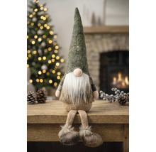 Sitzender Weihnachtsgnom mit spitzem Filzhut, langem weißen Bart und Schlenkerbeinen auf einem Holztisch in einer weihnachtlichen Umgebung.