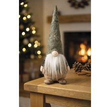 Weihnachtsgnom aus Filz mit Bart auf einem Holztisch in einem hellen Raum mit geschmücktem Weihnachtsbaum und Kamin.