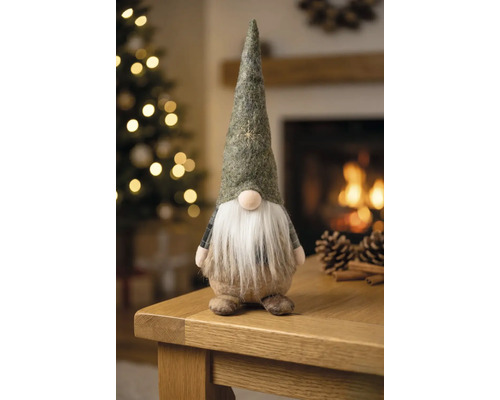 Weihnachtsgnom aus Filz mit Bart auf einem Holztisch in einem hellen Raum mit geschmücktem Weihnachtsbaum und Kamin.