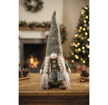 Stoff-Weihnachtsgnom mit langer Mütze, Zöpfen und Karorock auf Holztisch vor Kaminfeuer und beleuchtetem Weihnachtsbaum.