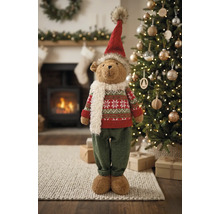 Weihnachts-Dekofigur Teddybär mit Mütze, Schal und Strickpullover vor einem Weihnachtsbaum und Kamin.