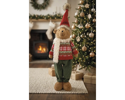 Weihnachts-Dekofigur Teddybär mit Mütze, Schal und Strickpullover vor einem Weihnachtsbaum und Kamin.