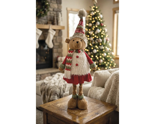 Weihnachts-Stoffbär in festlicher Kleidung auf einem Holztisch, im Hintergrund ein geschmückter Weihnachtsbaum und ein Kamin.