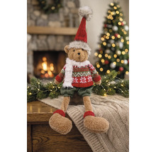 Plüschbär in weihnachtlicher Kleidung mit Mütze und Schal vor einem Kamin und einem geschmückten Weihnachtsbaum.
