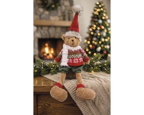 Plüschbär in weihnachtlicher Kleidung mit Mütze und Schal vor einem Kamin und einem geschmückten Weihnachtsbaum.