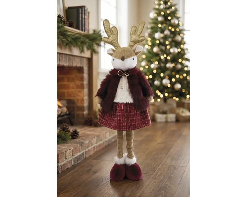 Plüsch-Weihnachtsfigur Rentier mit goldenem Geweih, rotem Kunstpelz und Rock, stehend im Wohnraum vor einem geschmückten Weihnachtsbaum.