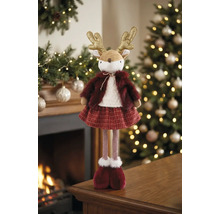 Dekorative Rentierfigur aus Plüsch und Strick im Winteroutfit vor einem beleuchteten Weihnachtsbaum und Kamin, festliche und warme Atmosphäre.