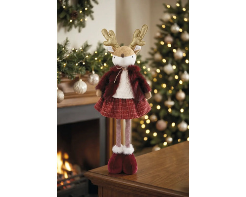 Dekorative Rentierfigur aus Plüsch und Strick im Winteroutfit vor einem beleuchteten Weihnachtsbaum und Kamin, festliche und warme Atmosphäre.