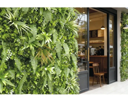 Vertikaler Garten mit Farnen und Kunstpflanzen neben einem gläsernen Café-Eingang mit schwarzem Rahmen.