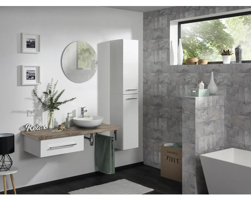 Modernes Badezimmer mit hängendem Waschtisch, weißem Hochschrank, rundem Spiegel und freistehender Badewanne vor grauen Fliesen wirkend.