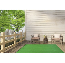 Grüner Kunstrasenteppich auf einer hellen Holzterrasse mit zwei Gartenstühlen und einem Holzzaun im Hintergrund.