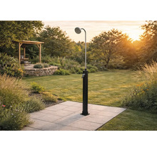 Solardusche im Garten auf Fliesen montiert, mit großem Duschkopf und Einhebelmischer, im Hintergrund Rasen und Gartenhaus.