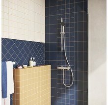 Moderne Dusche mit verchromtem Duschset auf dunkelblauen Fliesen, gelber Ablage und blauem Fischgrät-Fliesenmuster.